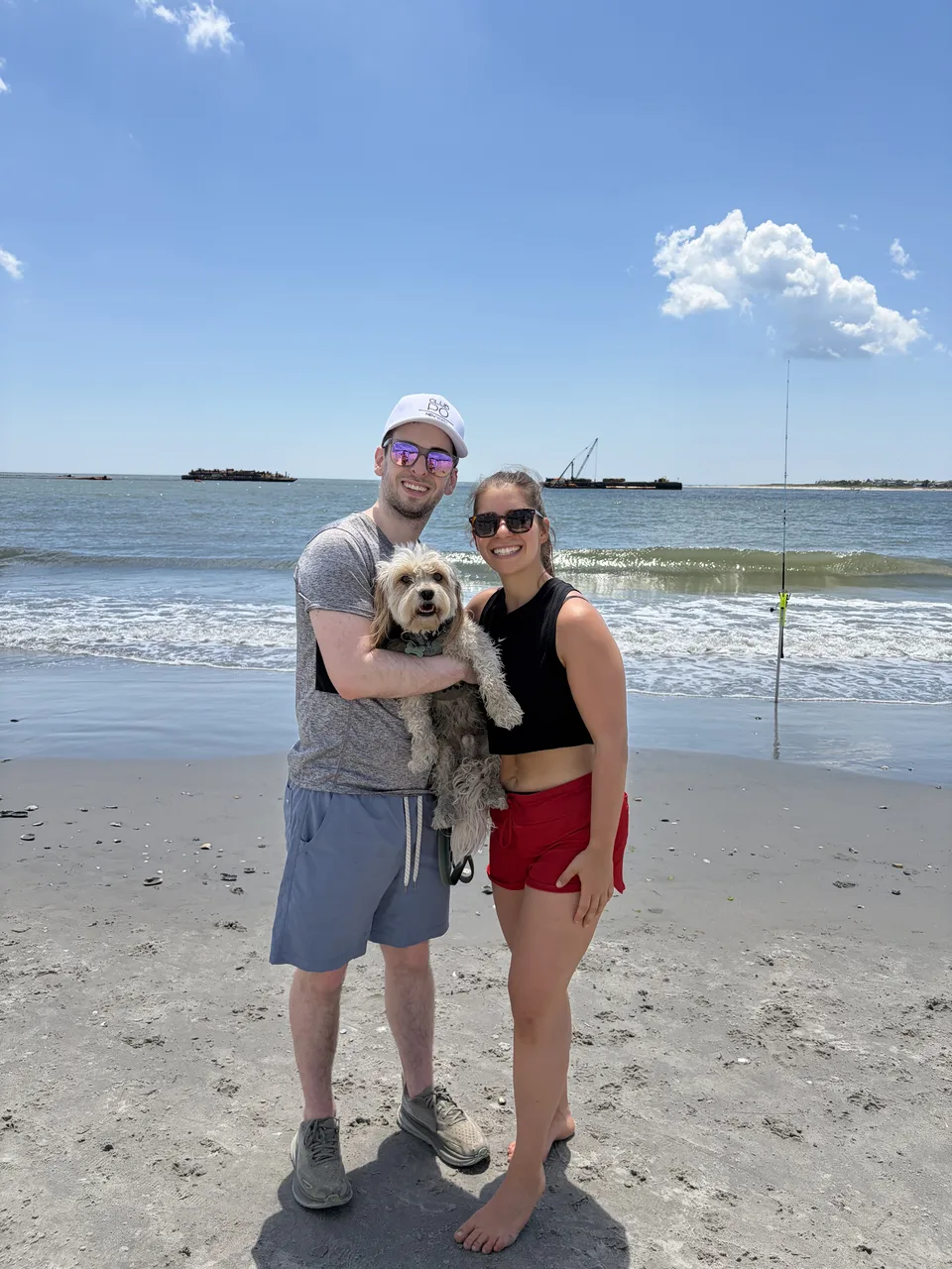 Leah and Justin at the beach holding Loki, the ocean behind them.